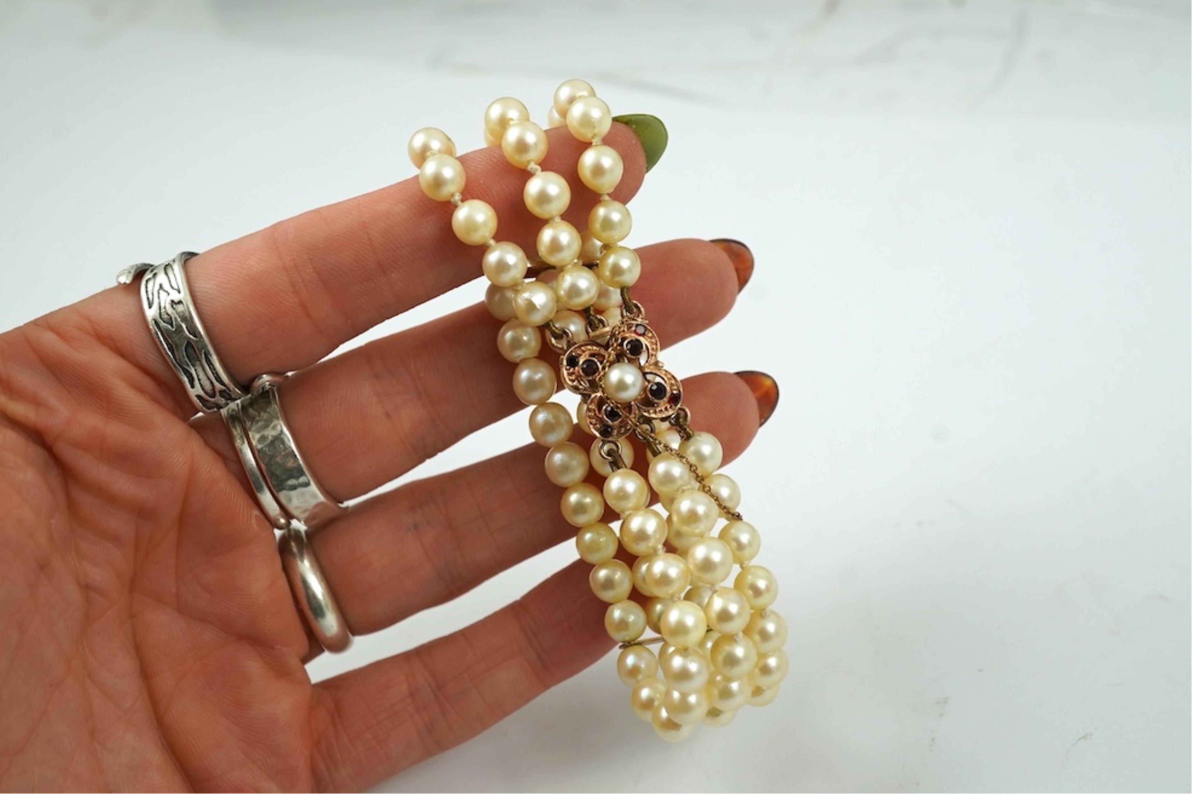 A triple strand cultured pearl bracelet, with a 9ct gold, garnet and cultured pearl cluster set clasp, 16cm.